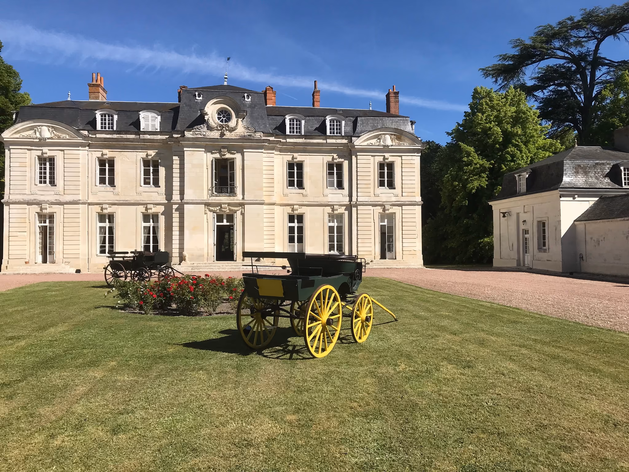 Façade principale du château de tuffeau vue de face avec une calèche sur la pelouse