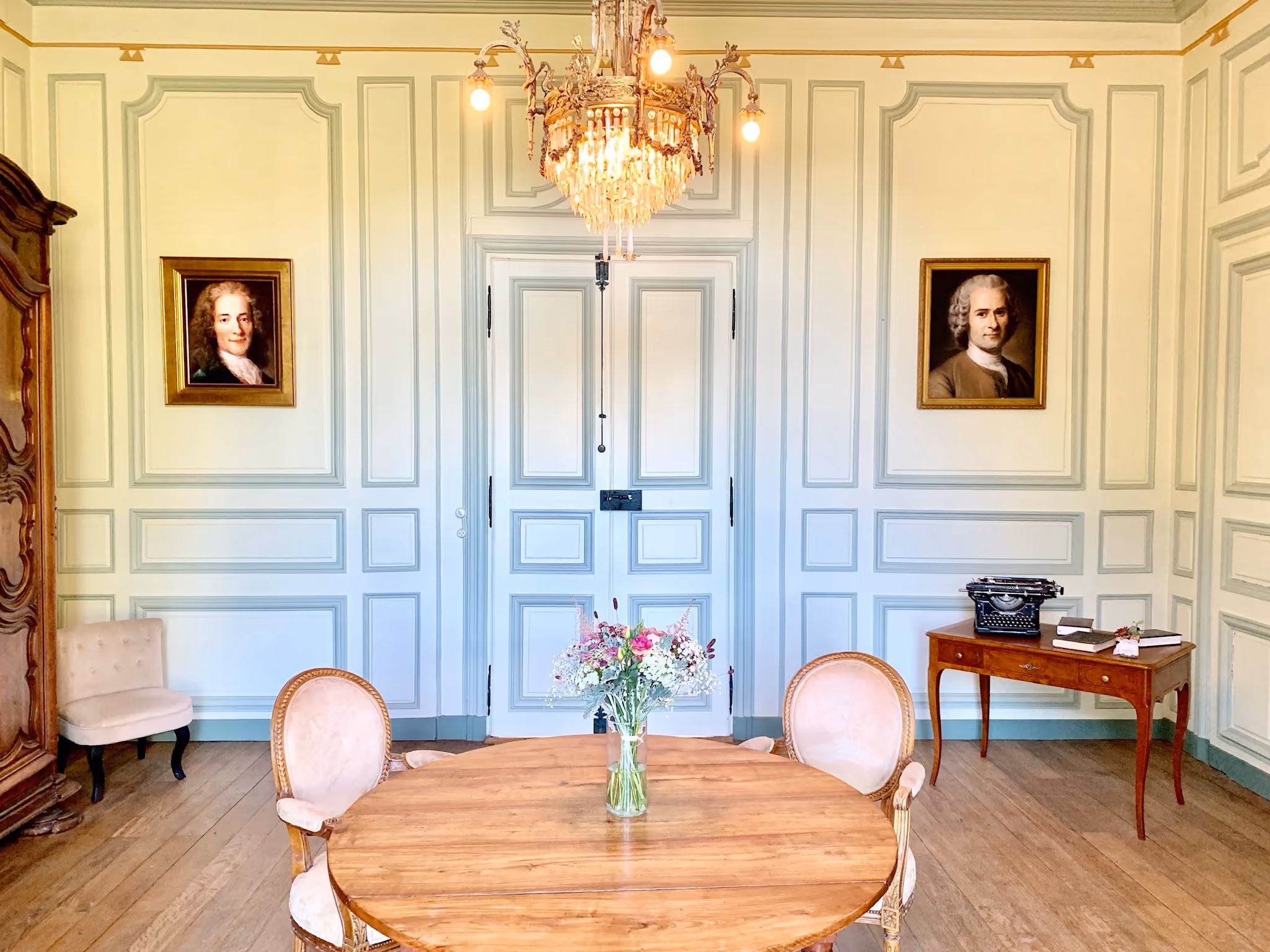 Salon aux boiseries bleu pâle avec portraits de Voltaire et Rousseau et lustre de cristal