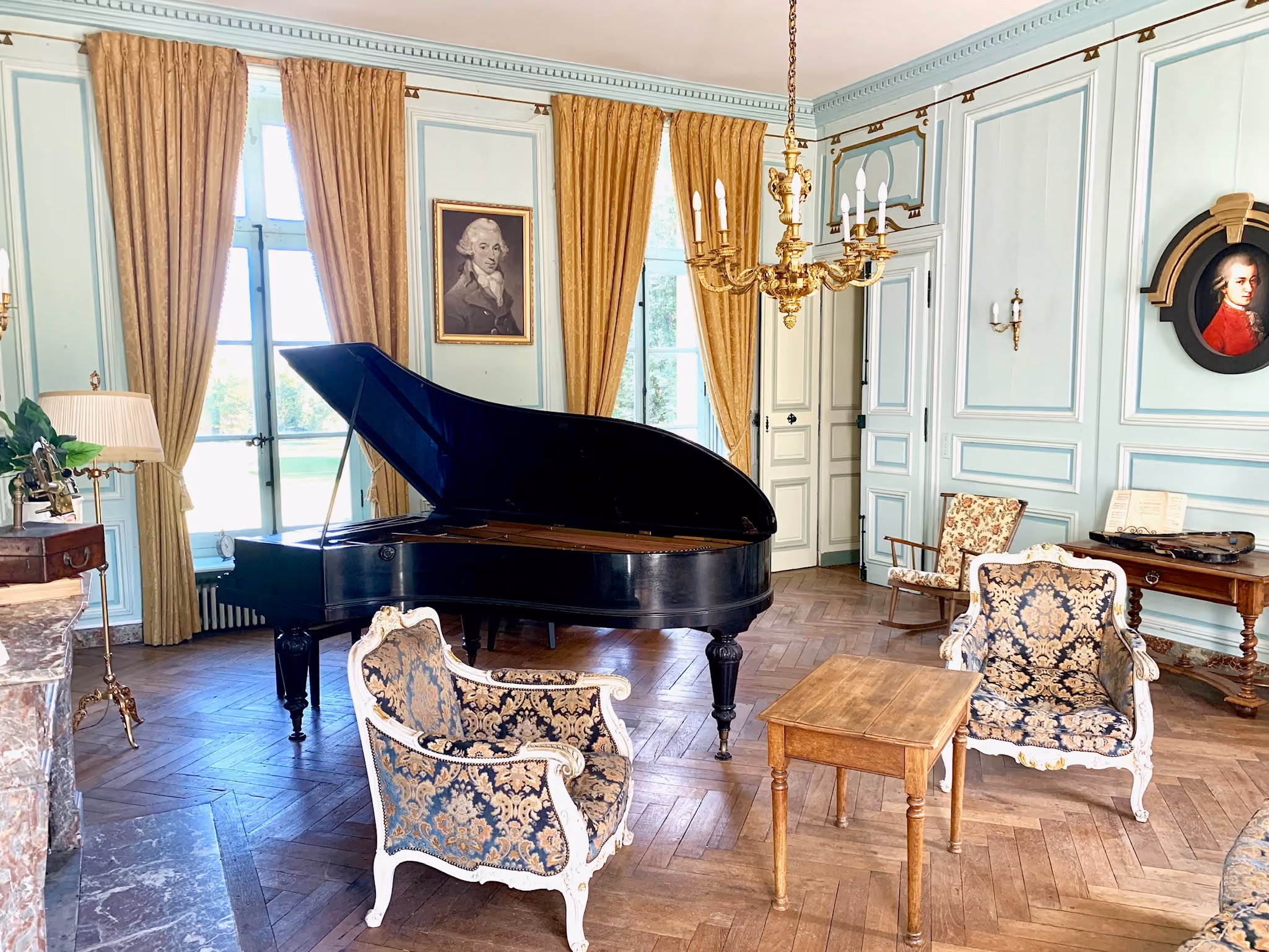 Salon de musique avec piano à queue, lustre doré et médaillon de Mozart aux murs